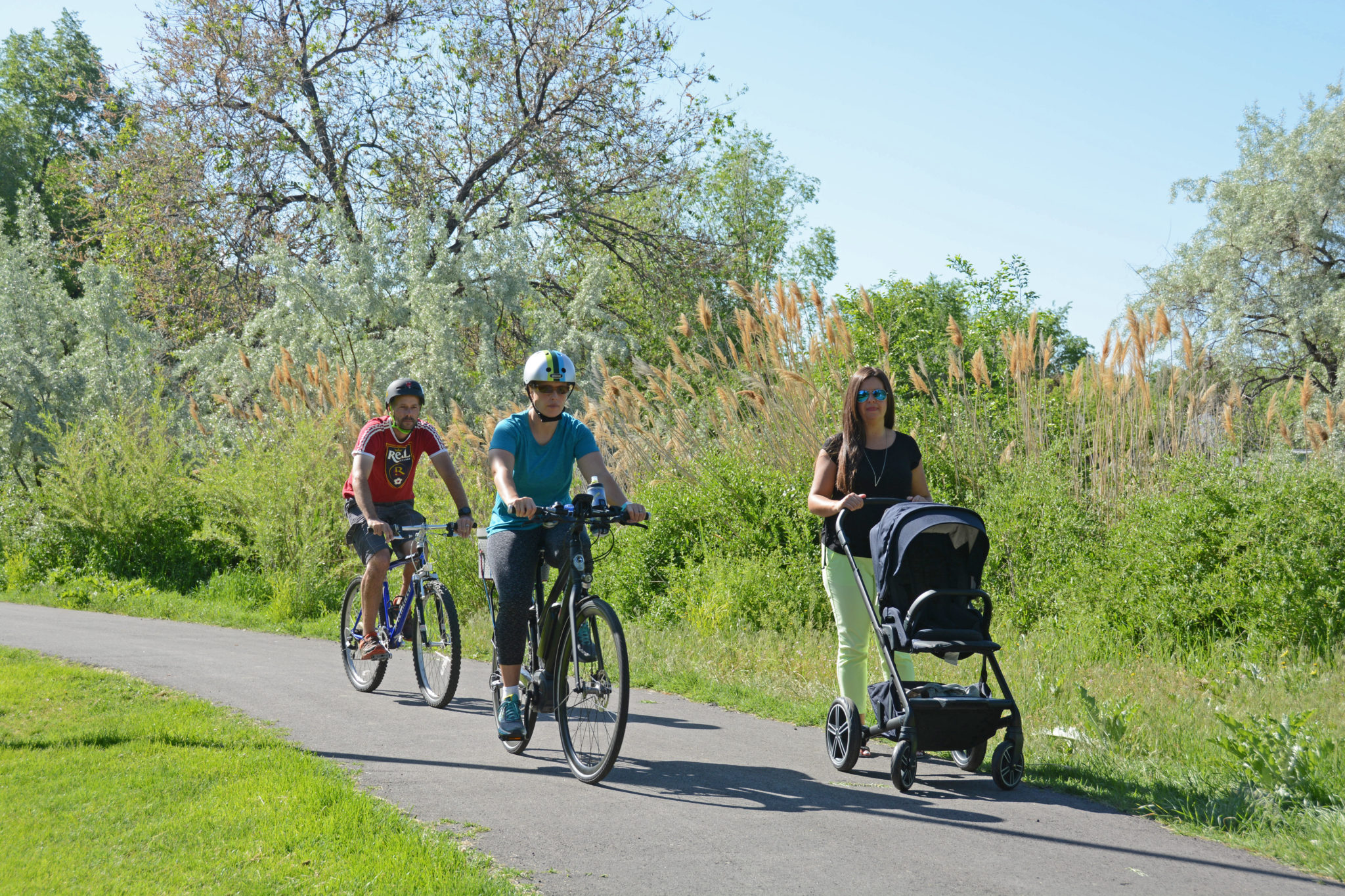 Bicyclists and a walker with a stroller utilize the Golden Spoke trail network (Jordan River Trail).